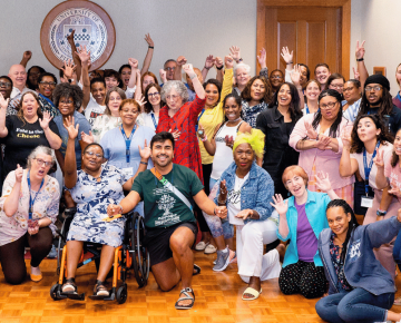 A diverse group of individuals smiling and waving at a racial equity consciousness training event