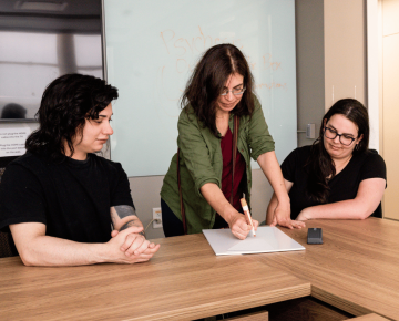 Dr. Nev Jones standing in a classroom with two students and pointing to a research paper