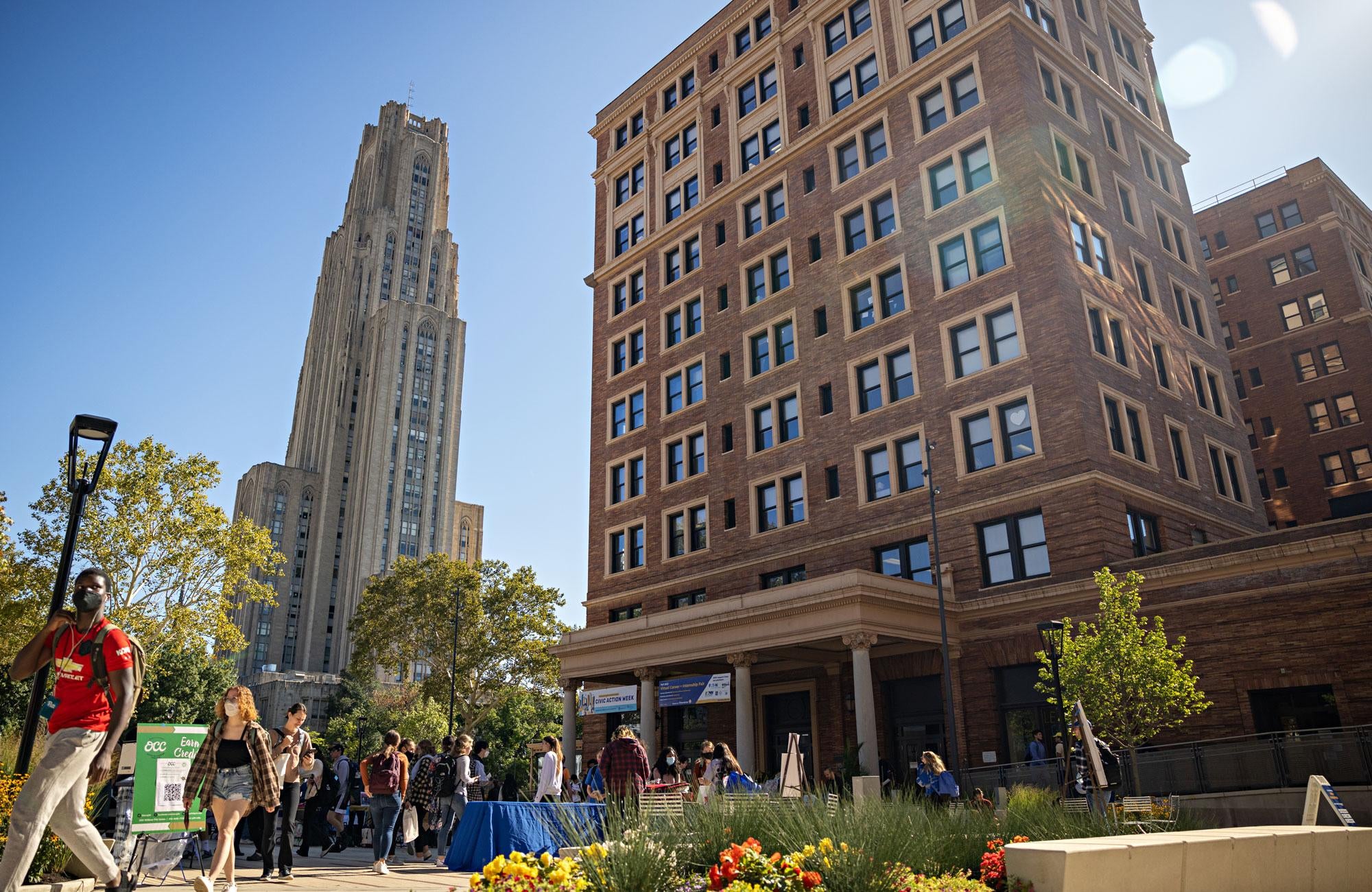 Students walk on campus with the Cathedral of Learning and William Pitt Union in the background.